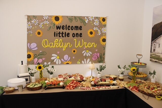 Welcome Little One Oaklyn Wren hand-painted baby shower banner displayed above a food table